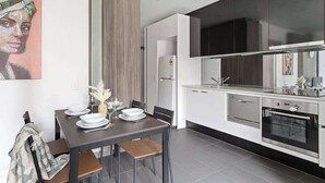 Una cocina moderna con armarios blancos, horno empotrado y comedor con mesa para cuatro.