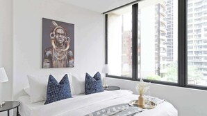 Una habitación de hotel moderna con una cama grande, vistas a la ciudad y un cuadro en la pared.