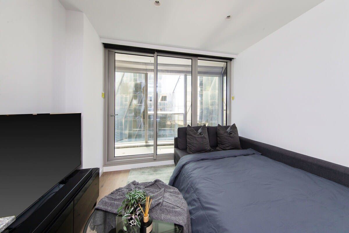 A modern bedroom with a large bed, a flat-screen TV, and a sliding glass door leading to a balcony.