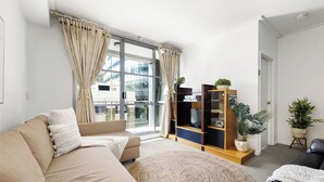 Un salon moderne avec un canapé beige, un tapis rond en fibres naturelles et un meuble de rangement en bois agrémenté de plantes.