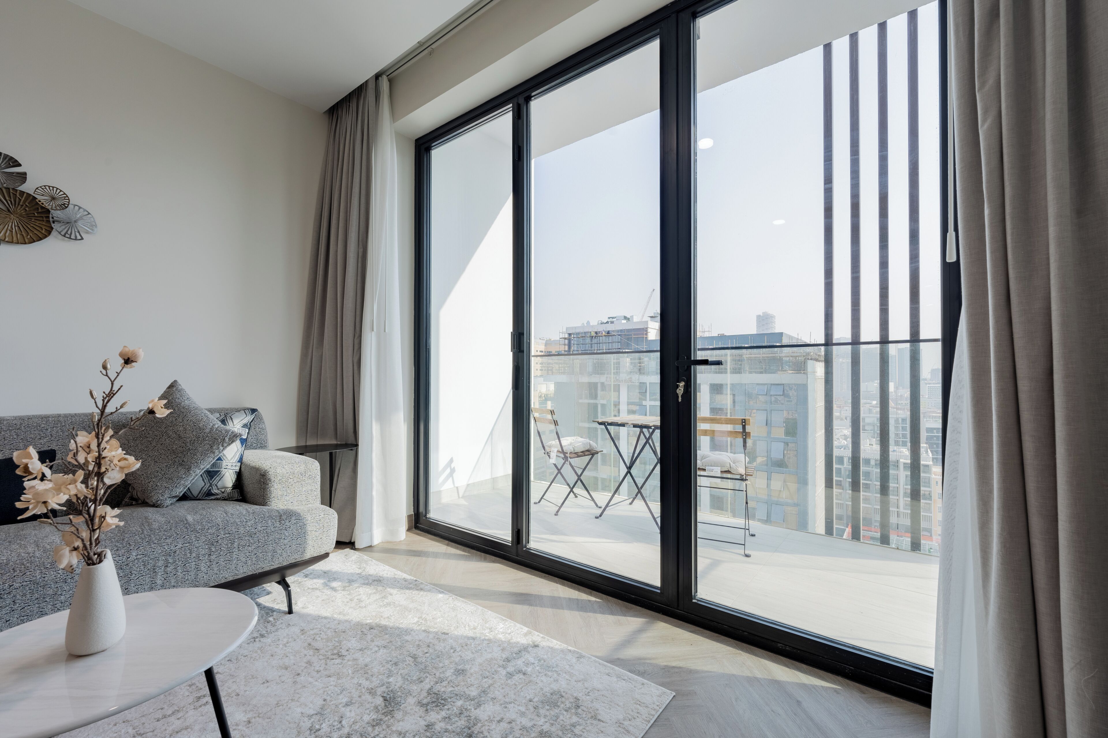 A modern living room with a grey sofa, a white coffee table, and a view of a balcony with a table and chairs.