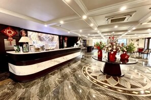 Zona de recepción de hotel con un mostrador de mármol, una mesa redonda con flores y un diseño de techo moderno.