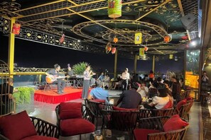 An indoor dining area with a stage for live music, red cushioned chairs, and a ceiling with decorative patterns. - MADELISE HOTEL&APARTMENT (Haiphong)