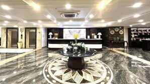 A hotel lobby with a reception desk, a central decorative table, and a patterned floor design. - MADELISE HOTEL&APARTMENT (Haiphong)
