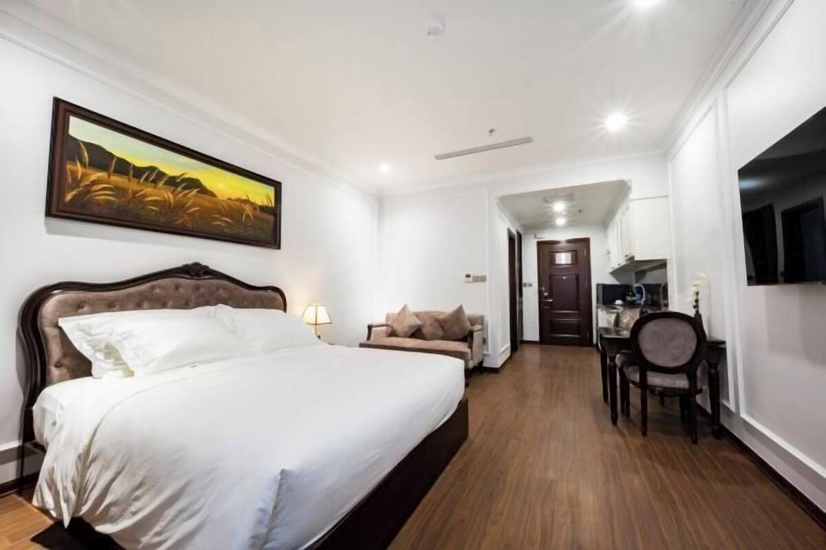 A hotel room with a large bed, a desk, a chair, and a TV mounted on the wall.