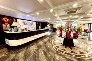 A hotel reception area with a marble counter, a round table with flowers, and a modern ceiling design. - MADELISE HOTEL&APARTMENT (Haiphong)