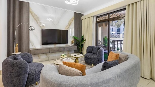 A modern living room with a flat-screen TV, grey sofas, a coffee table, and a large window with curtains.