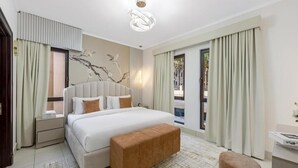 A modern hotel room with a large bed, a bedside table, a bench, and a view of the outside.