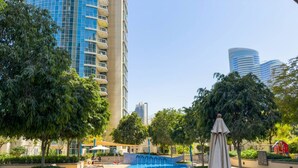 A swimming pool with a sunshade, surrounded by trees and modern buildings.