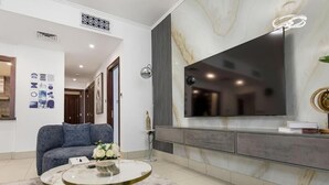 A modern living room with a large flat-screen TV mounted on a marble wall, a blue sofa, a round coffee table with a gold base, and a patterned rug.