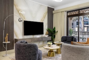 A modern living room with a flat-screen TV, grey upholstered sofas, and a marble wall.