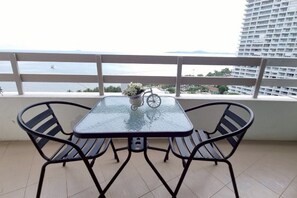 A balcony with a glass table and two chairs, overlooking a body of water and a cityscape. - Your Sea Beach condotel (Pattaya)