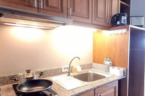 A kitchen with wooden cabinets, a granite countertop, a stove, a sink, and a microwave. - Your Sea Beach condotel (Pattaya)