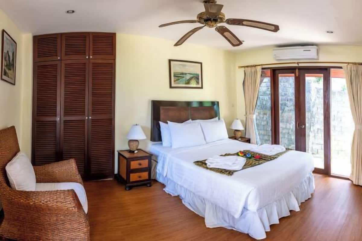 A bedroom with a bed, a nightstand, a chair, a ceiling fan, and a window with curtains.