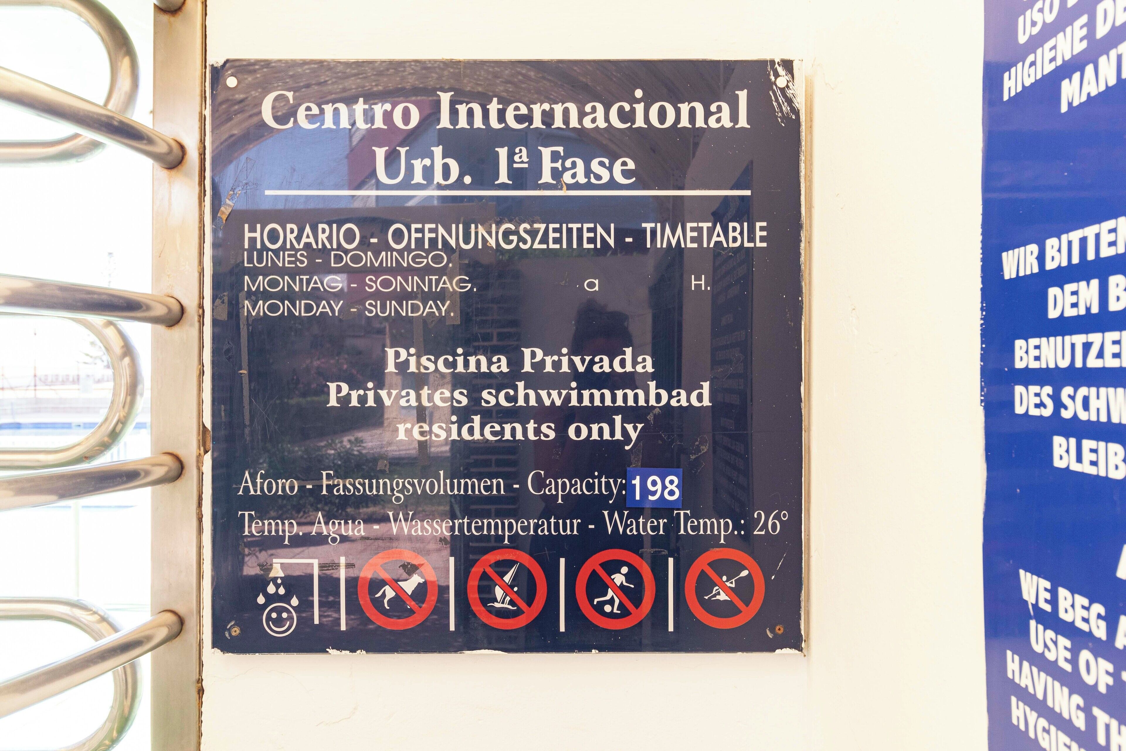 A sign for Centro Internacional Urb. 1ª Fase, indicating it is a private swimming pool for residents only with a capacity of 198 and a water temperature of 26°C.