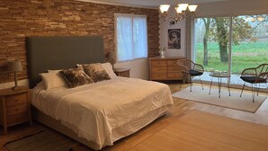A bedroom with a large bed, a wooden headboard, a nightstand, a dresser, and a view of the outdoors through a sliding glass door. - Chez PhiL (La Pomarède)