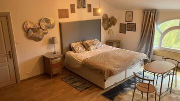A bedroom with a bed, bedside table, lamp, decorative wall art, and a window with curtains.