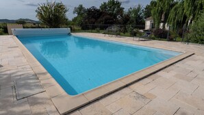 A rectangular swimming pool with a tiled deck, surrounded by a fence and trees. - Chez PhiL (La Pomarède)