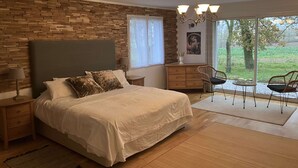 A bedroom with a large bed, a wooden headboard, a nightstand, a dresser, and a view of the outdoors through a glass door. - Chez PhiL (La Pomarède)