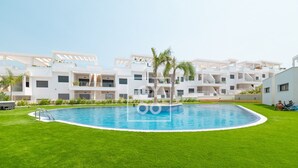 A modern hotel with a swimming pool surrounded by well-maintained grass and palm trees. - Nalia Horizon Penthouse, Outdoor living with solarium, BBQ, pool, hot tub - by OYOOSTAYS (Torrevieja)