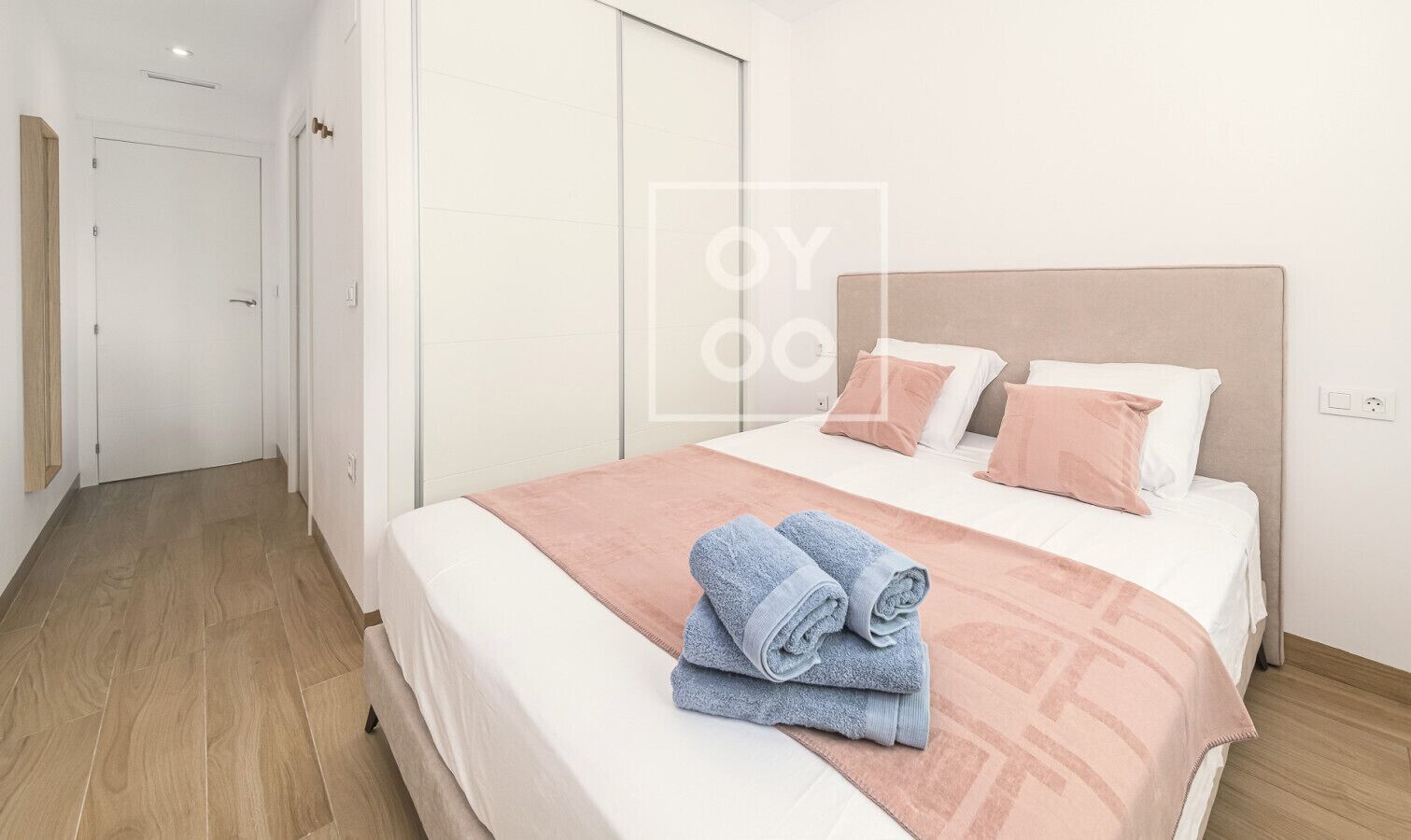 Una habitación de hotel con una cama, suelo de madera, una puerta blanca y un armario.