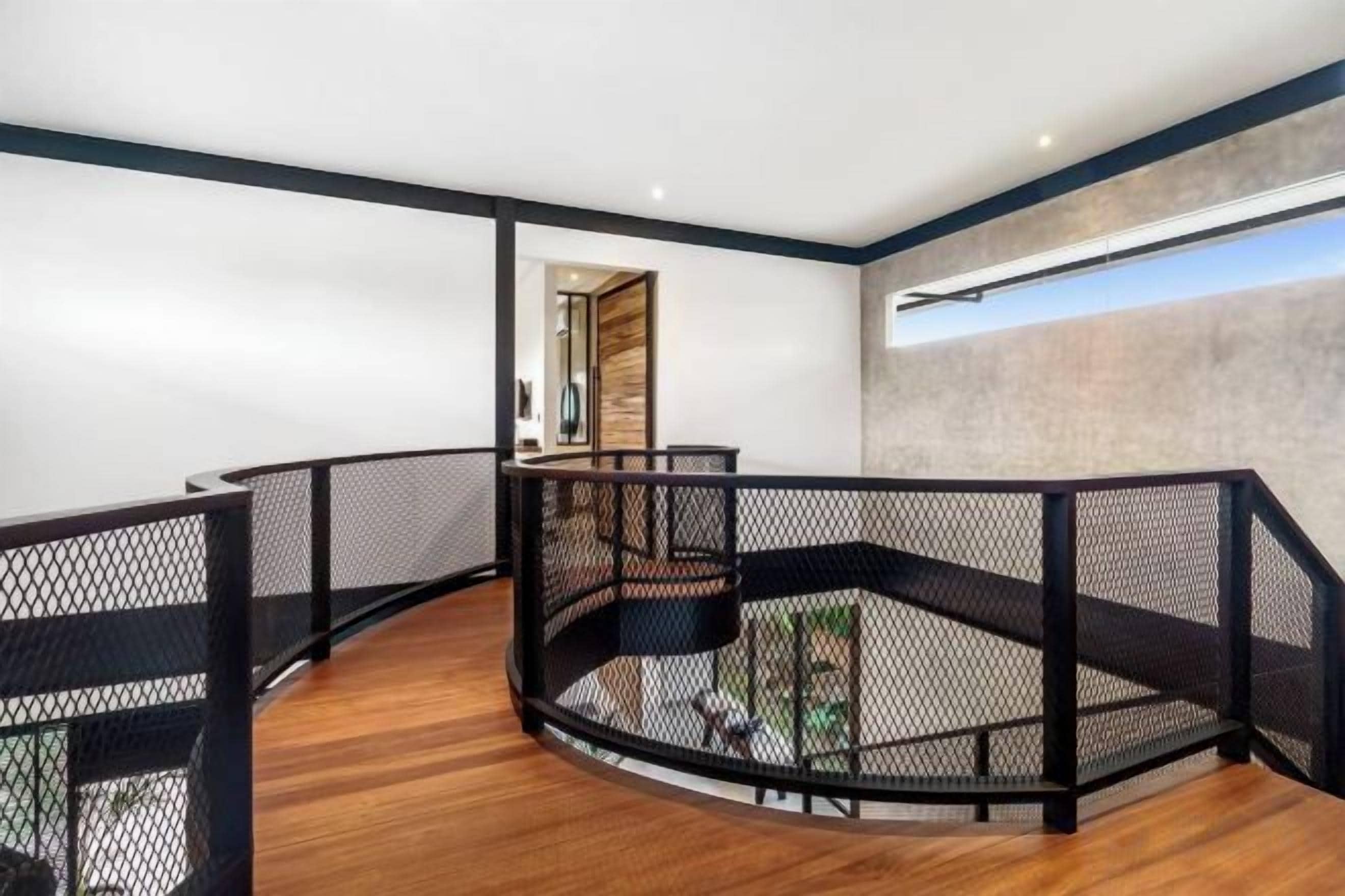 A modern interior with a curved staircase, black railings, and a view of the outdoors.