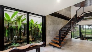 A modern interior with a staircase, a bench, and a large window with plants. - Villa Koma by BaliSuperHost (Bali)