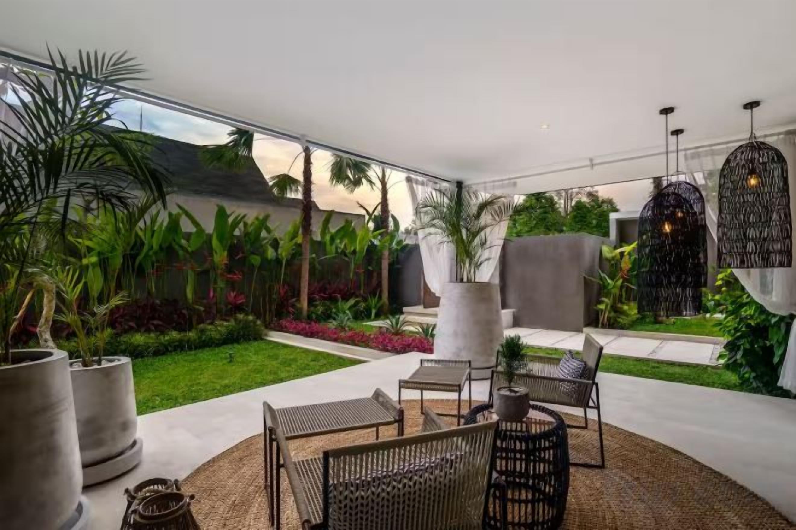 Un espacio moderno de estar al aire libre con vistas a un jardín exuberante, una planta grande en maceta y una lámpara colgante original.