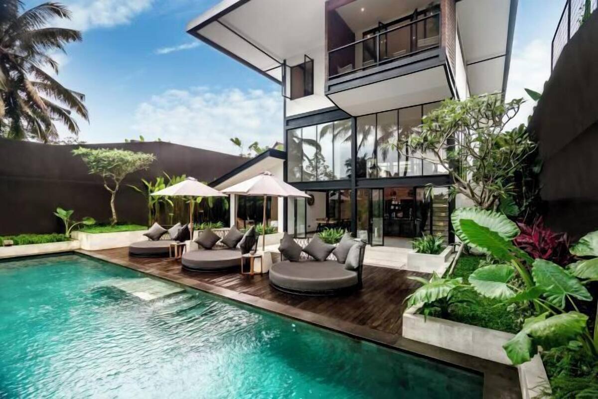 A modern two-story house with a swimming pool, outdoor seating, and lush greenery.