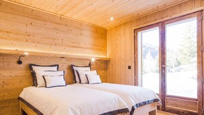 Ein Schlafzimmer mit Holzwänden, einem großen Bett, einem Nachttisch und einem Fenster mit Blick auf Bäume.