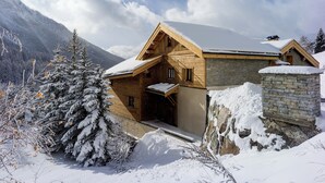 Eine Holzhütte mit Steinfundament, umgeben von schneebedeckten Bäumen und Bergen.