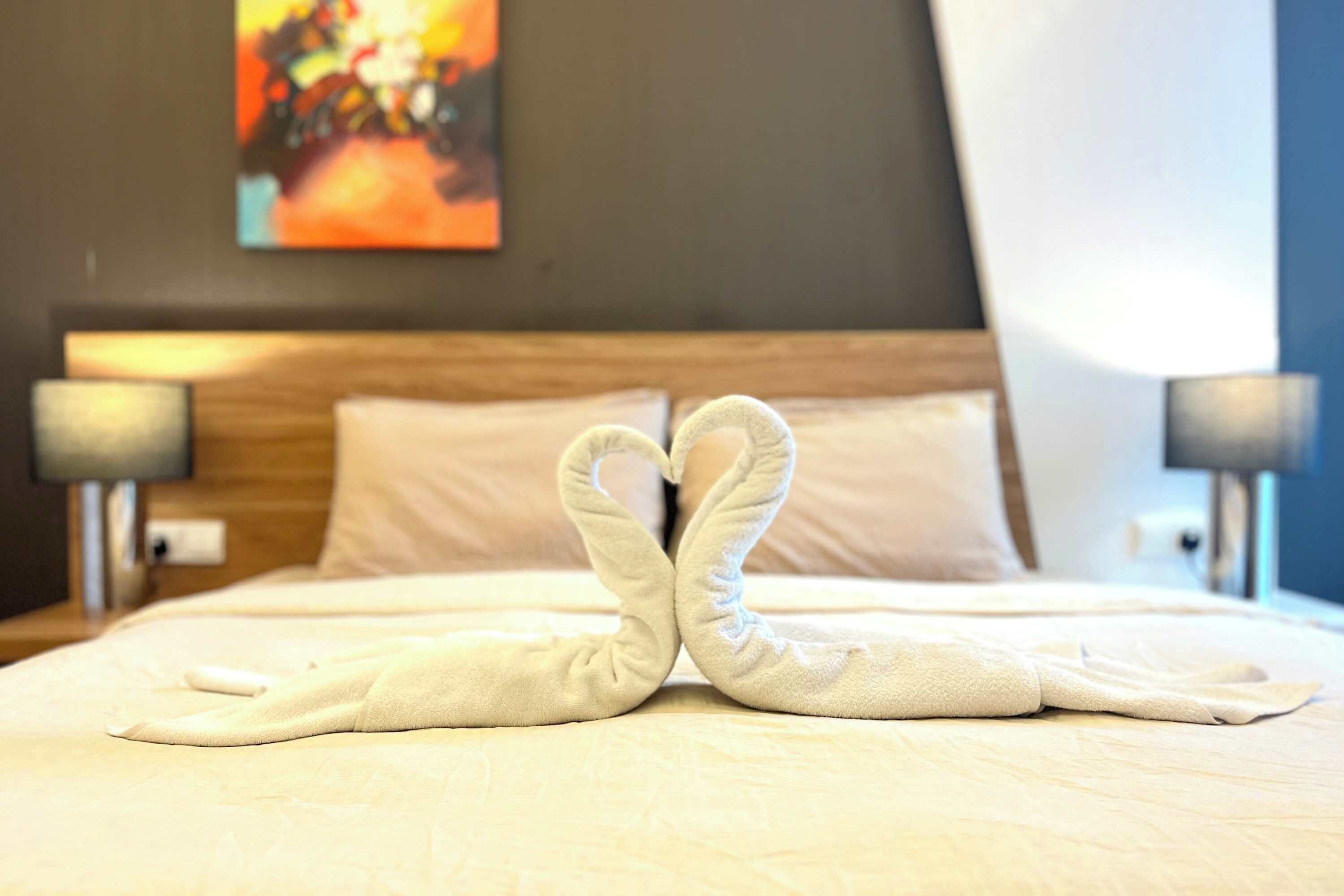 A neatly made bed with towels arranged in a heart shape.