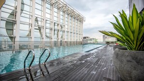 A rooftop pool with a wooden deck, surrounded by a glass facade building. - High Floor Suasana Suites 5 in JB City With Wifi (Johor Bahru)