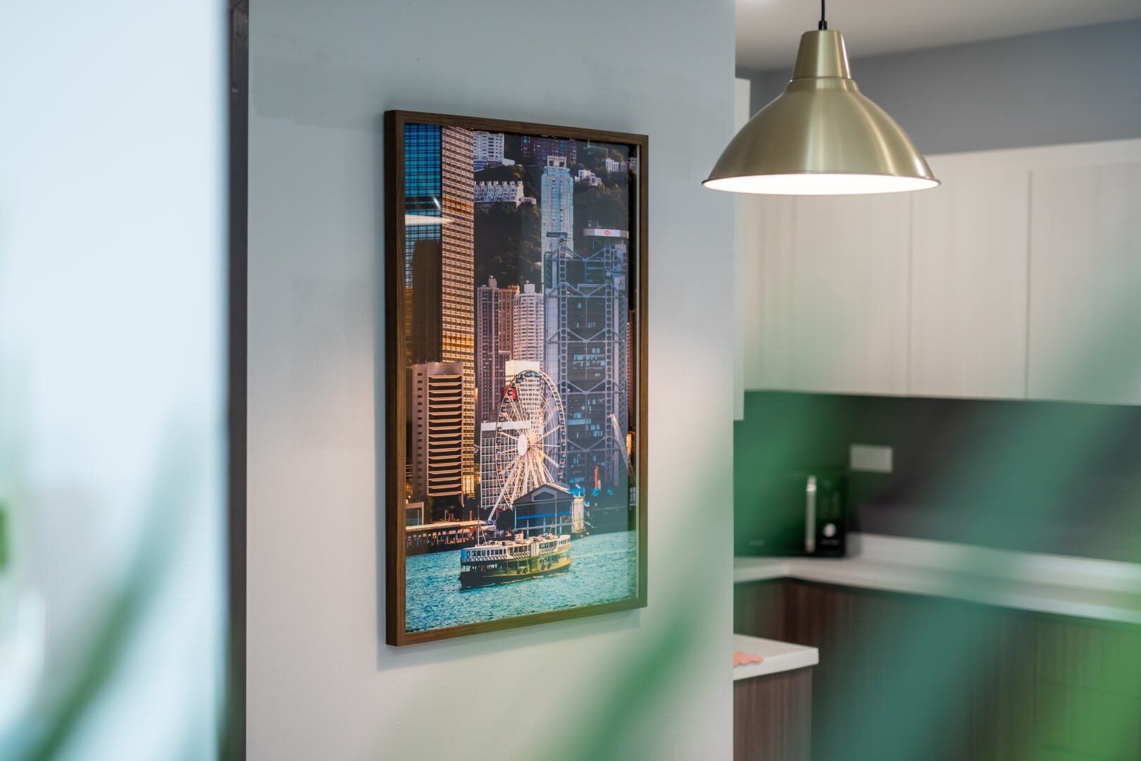 A framed cityscape artwork on a wall, a pendant light, and a kitchen area with cabinets and a countertop.