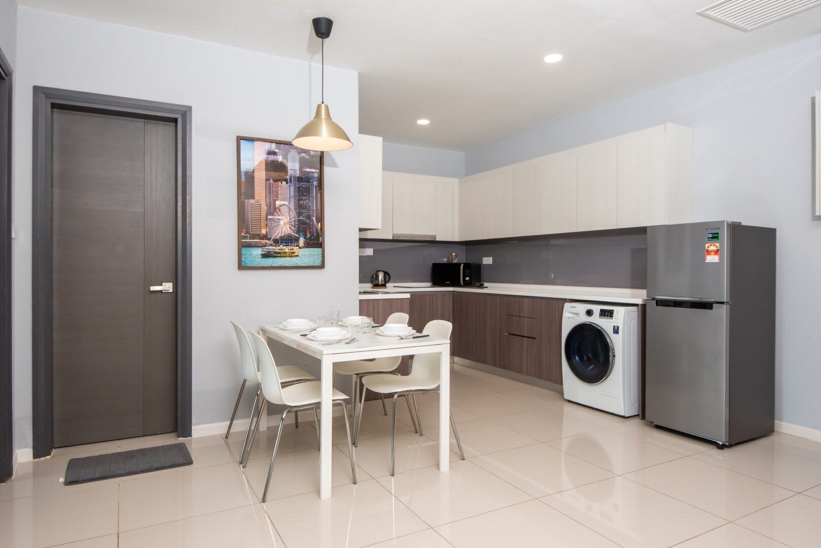 A modern kitchen with a built-in washing machine, a dining area with a white table and chairs, and a framed cityscape picture on the wall.