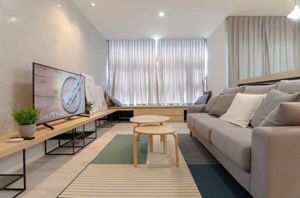 A modern living room with a sofa, a TV, a small table, and a window with curtains.