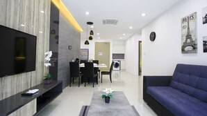 Una sala de estar moderna con un televisor de pantalla plana, un sofá, una zona de comedor con sillas y una cocina al fondo.