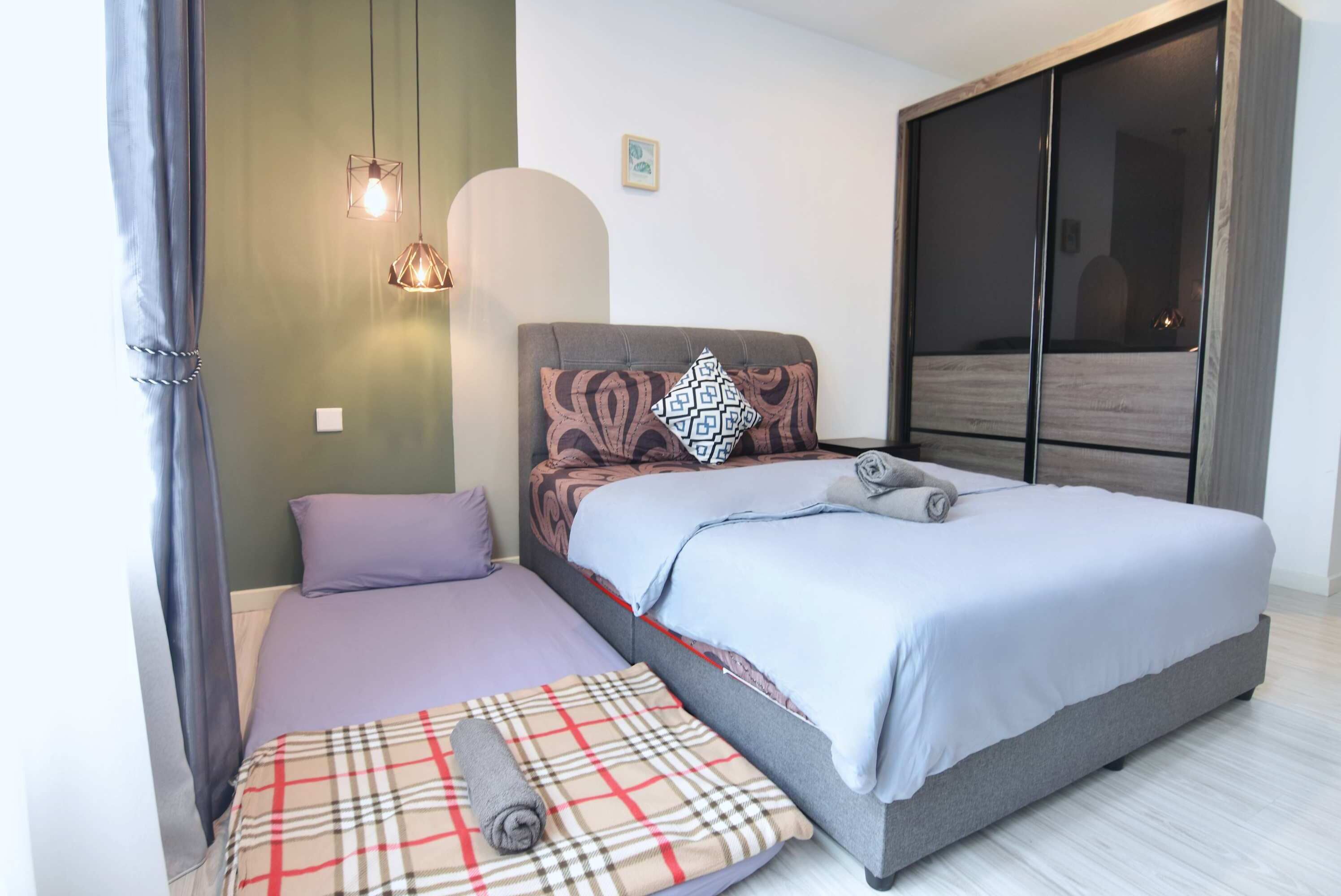 A bedroom with a large bed, a smaller bed, and a sofa bed. There are two pendant lights and a wall-mounted light.