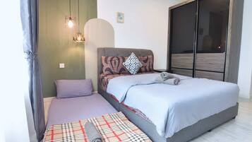 A bedroom with a large bed, a smaller bed, and a sofa bed. There are two pendant lights and a wall-mounted light.