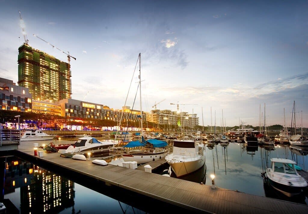 Un puerto deportivo con barcos amarrados, una grúa de construcción y edificios al fondo.