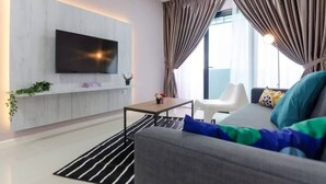 Una sala de estar moderna con un televisor de pantalla plana montado en una pared blanca, un sofá gris con cojines de colores, una mesita pequeña y una alfombra a rayas negras y blancas.