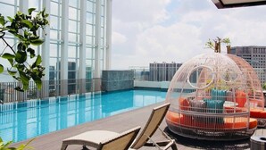 Un área de piscina en la azotea con vistas despejadas del horizonte de la ciudad, un amplio ventanal y una estructura esférica de asientos singular.