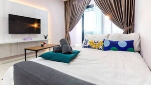 Una habitación de hotel moderna con una cama grande, un televisor de pantalla plana en la pared, una mesita y una ventana con cortinas.