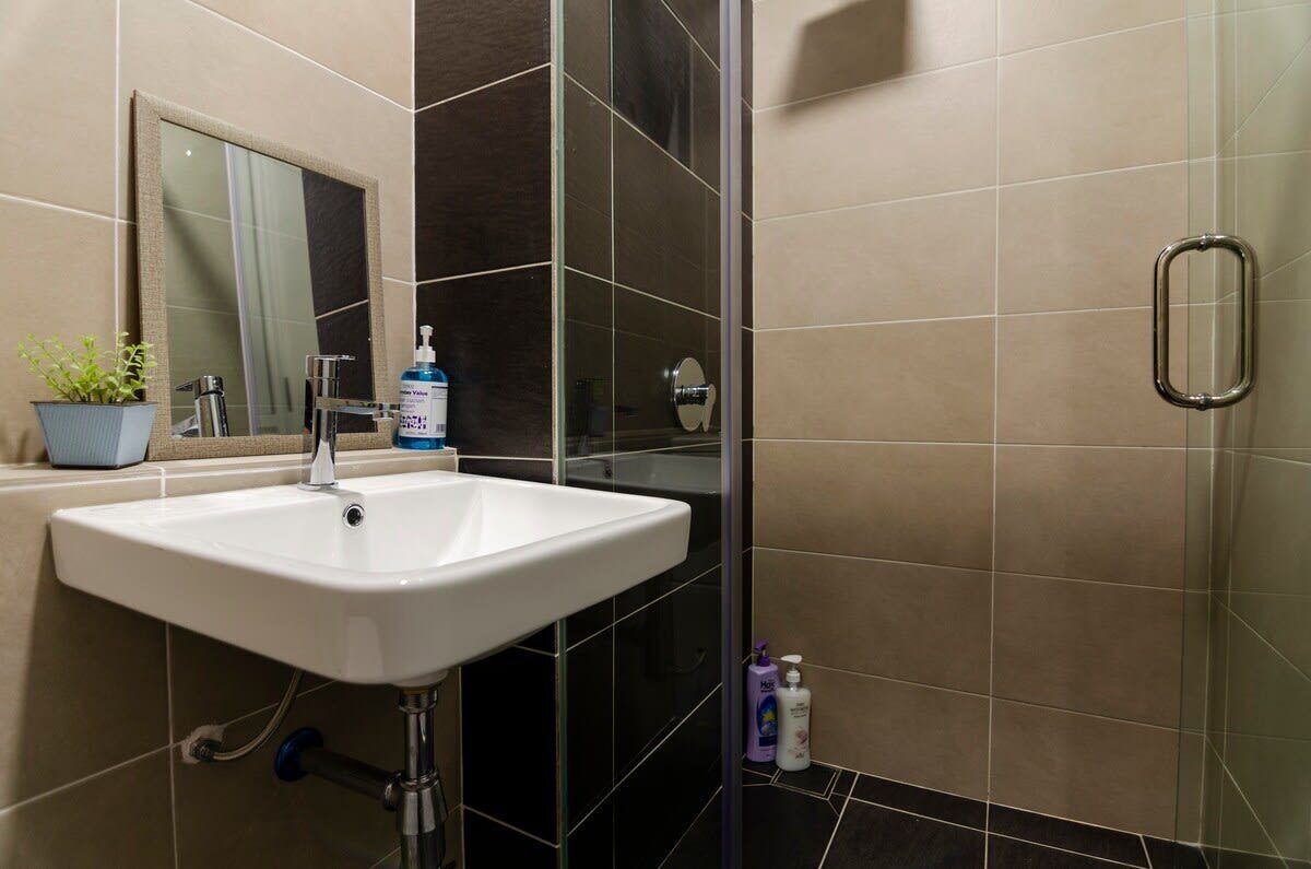 Ein Badezimmer mit einem weißen Waschbecken, einem Spiegel, einer Glasdusche und einem Blumentopf.