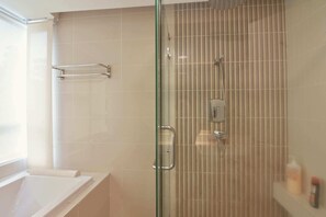 A modern bathroom with a glass shower enclosure, a white bathtub, and a towel rack.