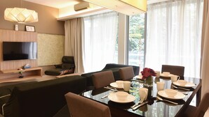 A modern hotel room with a dining area, a sofa, a TV, and a large window with curtains. - Pet Friendly, 3BR Apt KL, Bathtub & Parking (Kuala Lumpur)