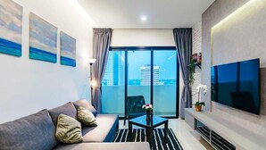 A modern living room with a sofa, a coffee table, and a TV. There are curtains, a plant, and a view of buildings through large windows. - A Stylish & Cozy Suite at Suasana JB 03 (Johor Bahru)