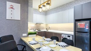 A modern kitchen with a dining area, featuring a long table set for four, a built-in oven, and a refrigerator. - A Stylish & Cozy Suite at Suasana JB 03 (Johor Bahru)