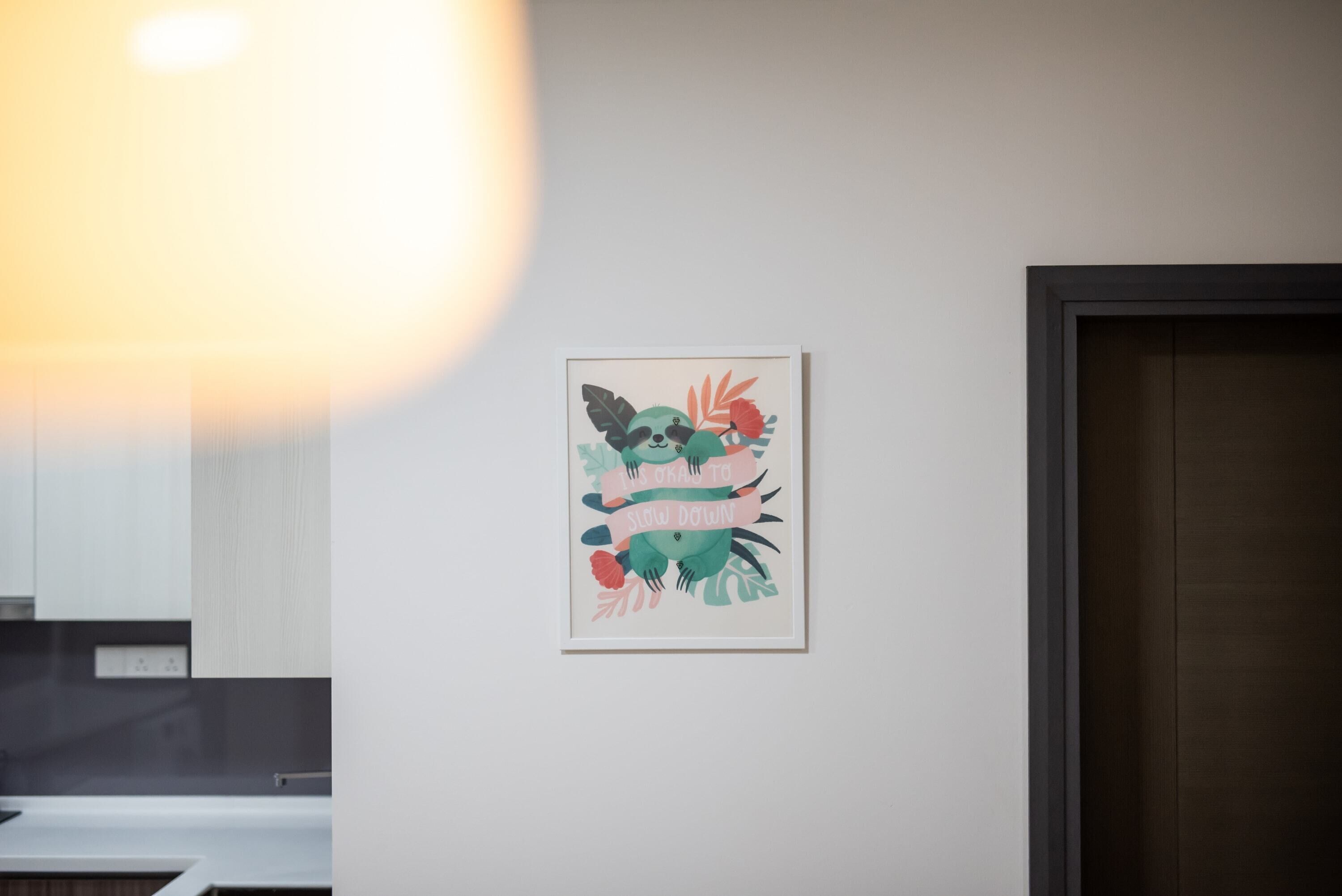 A framed artwork with a koala and leaves on a white wall in a room with a dark door and a white countertop.