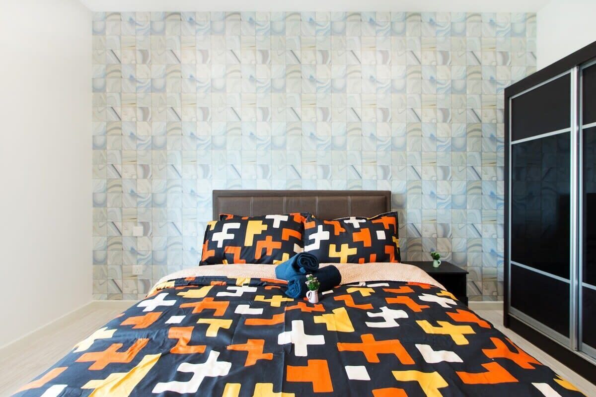 A bedroom with a patterned bedspread, a headboard, a nightstand, and a large window.